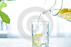 Pouring a glass of water with lemon, ice and mint on a white table