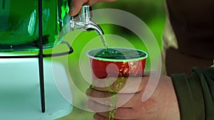 Pouring of green lemonade in a plastic cup in slow motion