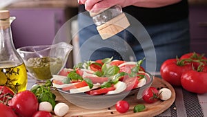 pouring grinded pepper on caprese salad - mozzarella cheese balls, sliced cherry tomatoes and basil