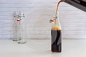 Pouring homemade cold brew coffee from glass jar to glass bottle