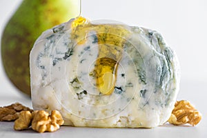 Pouring honey on blue cheese dorblu or gorgonzola with pear and walnuts on white background. Close up