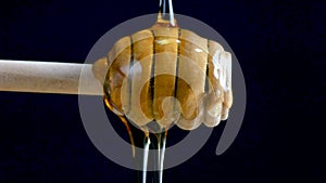 Pouring honey to a dripper stick against the black background
