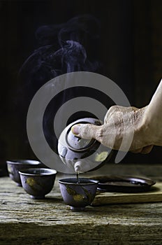 pouring hot tea from a teapot into a  cup on the old wood table a dark wood background