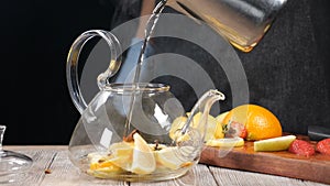 Pouring hot water into teapot with sliced fruit. Glass teapot with orange and lemon inside. Tea brewing Slow motion. Hot