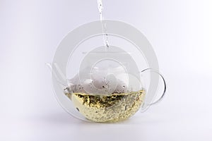 Pouring hot water to the glass teapot with herbal tea, isolated on white