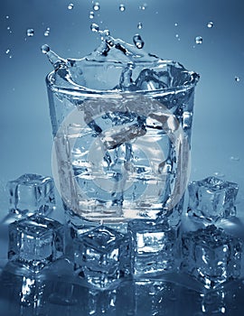 Pouring ice cube into drink glass of water.