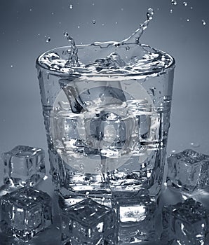 Pouring ice cube into drink glass of water. splashing water.