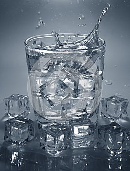 Pouring ice cube into drink glass of water. splashing water.