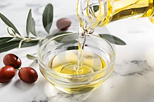 Pouring with jojoba oil from jug into bowl on table