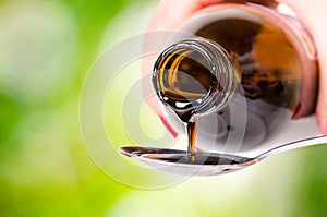 Pouring a liquid on a spoon. Natural green background. Pharmacy and healthy background. Medicine. Cough and cold drug.