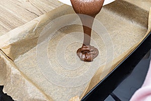 Pouring a liquid thick mass of cocoa dough onto a baking sheet lined with baking paper.