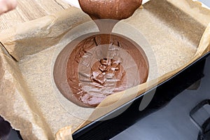 Pouring a liquid thick mass of cocoa dough onto a baking sheet lined with baking paper.