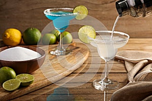 Pouring Margarita cocktail with lime and salt on wooden table background. Cocktails drink concept