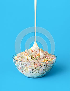 Pouring mayo over oliveir salad, minimalist on a blue background