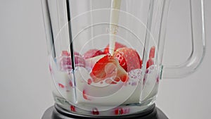 Pouring milk into blender with strawberry for cooking milkshake. Slow motion. Smoothie