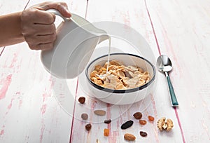 Pouring milk on a bowl of cornflakes , hazelnut, dry apricot, w