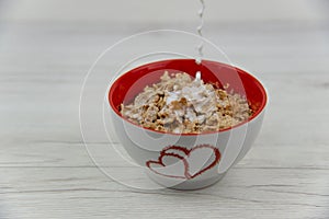 Pouring milk into a cereal bowl, on the white wood tabl