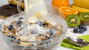 Pouring milk on cereals flakes and fruits for breakfast in slow motion