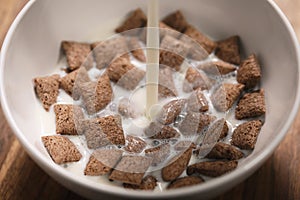 Pouring milk into chcolate cereal pillow in white bowl on table