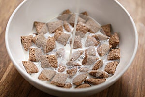 Pouring milk into chcolate cereal pillow in white bowl on table