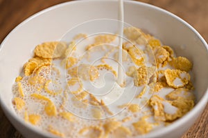 Pouring milk into corn flakes in white bowl closeup