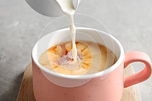 Pouring milk into cup of black tea on gray table