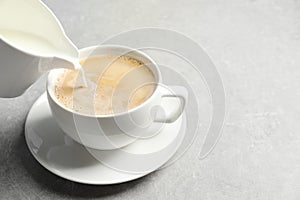 Pouring milk into cup of hot coffee on grey table, space for text