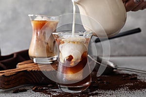 Pouring of milk into glass with cold coffee on grey table