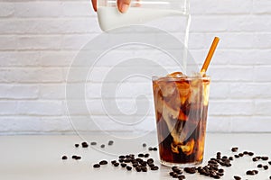 Pouring milk into a glass of homemade cold brew coffee on white