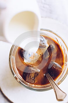 Pouring milk from a jug to a glass of espresso ice cubes