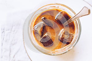 Pouring milk from a jug to a glass of espresso ice cubes