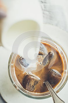 Pouring milk from a jug to a glass of espresso ice cubes