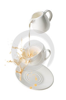 pouring milk and splashing milk tea from flying cup and saucer isolated on white