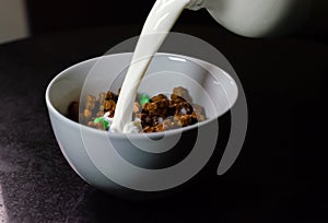Pouring milk on a white bowl with chocolate cereal 2 photo