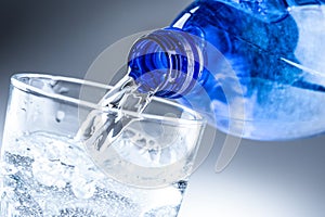 Pouring mineral water from blue bottle into clear glass on abstract grey background