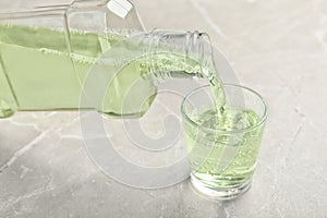 Pouring mouthwash in glass on light background