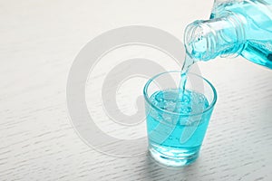 Pouring mouthwash in glass and space for text on wooden background