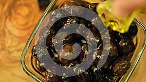 Pouring natural olive oil on black olives, close up, top view