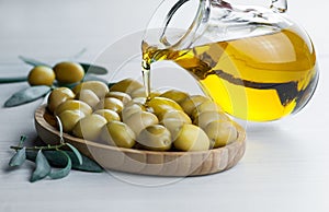 Pouring olive oil from bottle into glass on raw turkish green olives in bamboo bowl