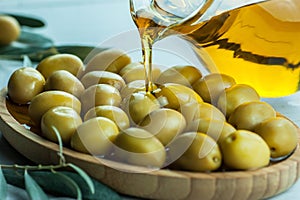 Pouring olive oil from bottle into glass on raw turkish green olives in bamboo bowl