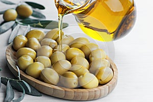 Pouring olive oil from bottle into glass on raw turkish green olives in bamboo bowl