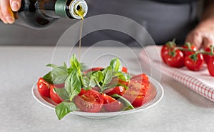 Pouring olive oil in a bottle over a cherry tomato salad with basil leaf