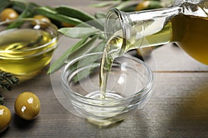 Pouring olive oil into bowl and olives on wooden table, closeup. Healthy cooking