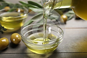 Pouring olive oil into bowl and olives on wooden table, closeup. Healthy cooking