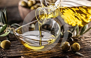 Pouring olive oil from carafe to the glass bowl and in background are olive branches put on table