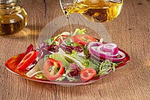 Pouring olive oil from glass pitcher over fresh vegetable salad in bowl