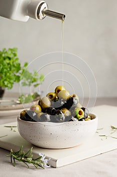 Pouring olive oil over green and black olives in a bowl