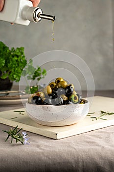 Pouring olive oil over green and black olives in a bowl