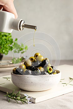 Pouring olive oil over green and black olives in a bowl