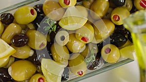 Pouring Olive Oil Over Olive Salad with Green and Black Olives and Lemon, Top View